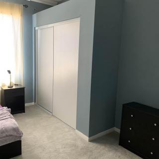 A minimalist bedroom with a bed, nightstand, dresser, and a sliding closet door.
