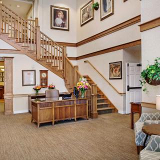 A welcoming lobby area featuring a wooden staircase, reception desk, and comfortable seating, adorned with artwork and plants.
