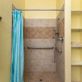 A shower area with a blue curtain, tiled walls, and grab bars for safety.