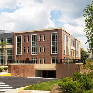 A modern brick building featuring large windows and a parking garage entrance beneath, set against a partly cloudy sky.