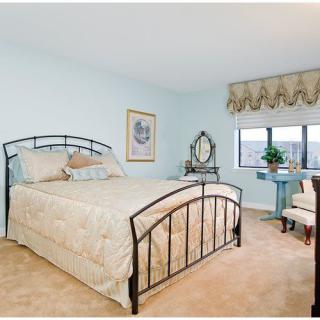 A cozy bedroom with a metal-framed bed, a window with drapes, and a small sitting area.