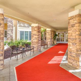 A red carpet leads through a covered entrance with stone columns and outdoor seating.