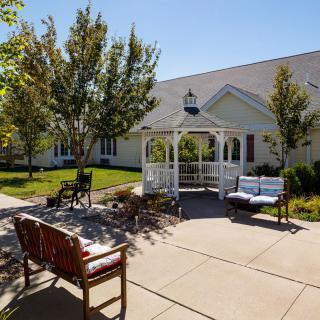 A sunny outdoor patio with a gazebo and benches surrounded by trees.