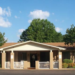 A single-story house with a front porch, surrounded by trees under a clear sky.