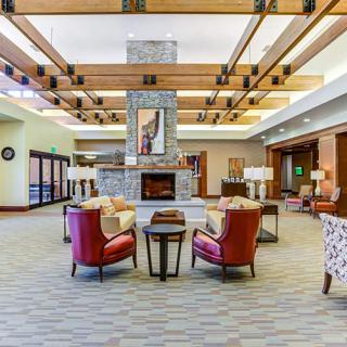 A spacious and elegantly designed lobby featuring comfortable seating, a central fireplace, and wooden beam ceilings.