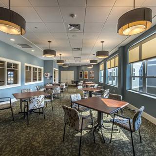 A modern dining room with neatly arranged tables and chairs, featuring large windows and contemporary lighting fixtures.