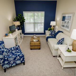 A cozy living room with a blue accent wall, featuring a white sofa, patterned armchair, and stylish decor.