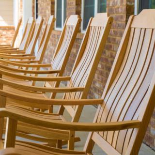 A row of wooden rocking chairs lined up on a porch beside a brick wall.