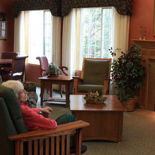 Two people sitting in a cozy living room with a fireplace and large windows.