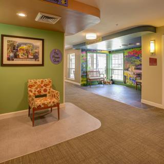 A warmly decorated lobby area featuring a floral-patterned chair, artwork on the wall, and colorful accents near large windows.