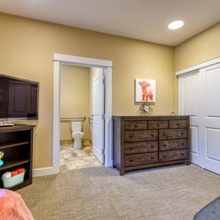 A cozy bedroom with a dresser, TV stand, and an adjoining bathroom.
