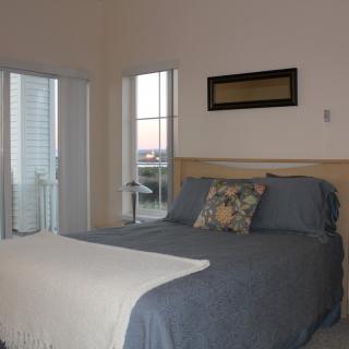 A cozy bedroom with a neatly made bed and large windows.