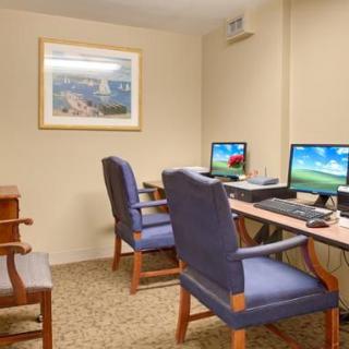 A small office with two computers on desks and blue chairs, featuring a wall painting.