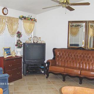 A cozy living room with a vintage leather sofa, an old CRT TV, decorative curtains, and mirrors on the wall.