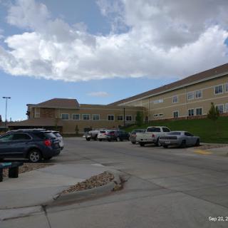 A view of a large building with a parking lot filled with vehicles under a partly cloudy sky.