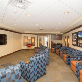 A spacious waiting room featuring patterned chairs arranged along the walls, with framed artwork and a large television mounted on one side.