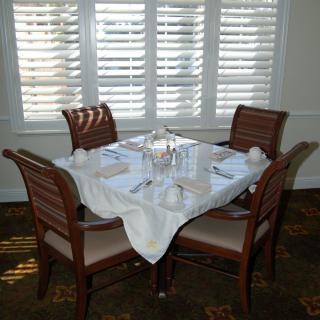 A neatly set dining table for four near a window with shutters.