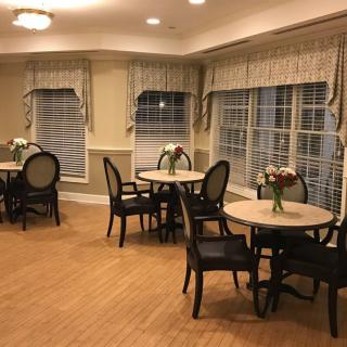 A cozy dining area with neatly arranged tables and chairs, adorned with floral centerpieces, under soft lighting.