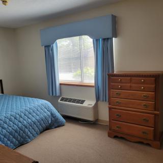 A bedroom with blue bedding and curtains, featuring a wooden dresser and a window.