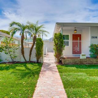 A charming house with a red door, surrounded by a lush front yard and palm trees.