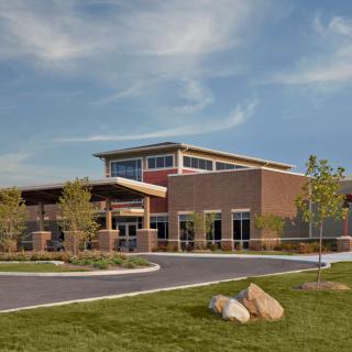 A modern school building with a brick exterior surrounded by landscaped grounds under a clear blue sky.