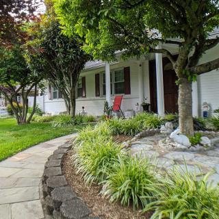 A beautifully landscaped front yard with a garden path leading to a porch adorned with chairs.