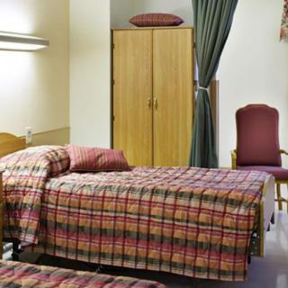 A hospital room with two beds, a wardrobe, and a chair.