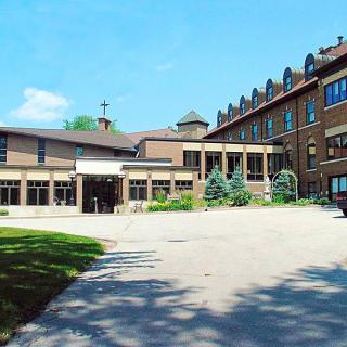 A large brick building with a driveway and landscaped greenery under a clear blue sky.