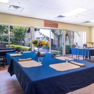A cozy dining area featuring blue table settings and vibrant floral arrangements, illuminated by natural light.