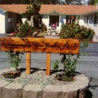 A wooden sign displayed in a landscaped garden area in front of a house.