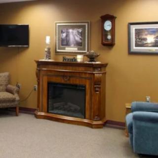 A cozy living room with a wooden fireplace, armchairs, and wall decorations.