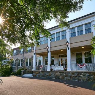 A large building with white columns and a porch, surrounded by trees, illuminated by sunlight.