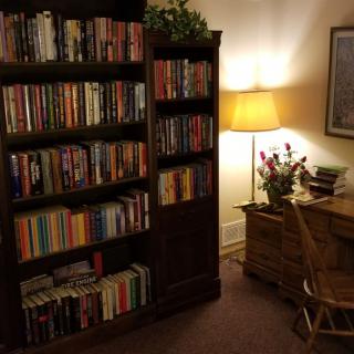 A cozy reading corner with a bookshelf filled with books, a desk, a chair, and a warm lamp.
