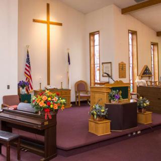Interior of a church displaying the altar with floral arrangements and flags.