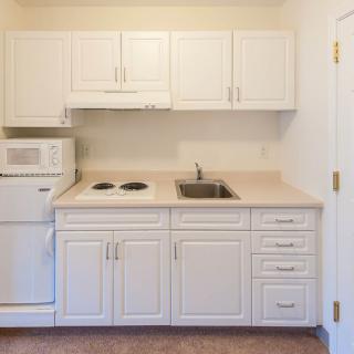 A compact kitchen area with white cabinets, a microwave, stovetop, and sink.