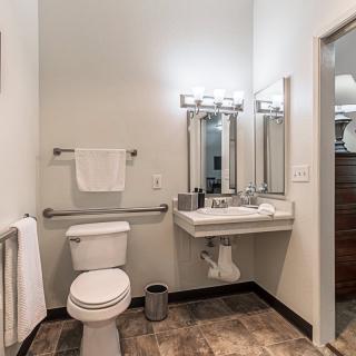 A modern bathroom with a toilet, sink, and mirror, featuring contemporary lighting and tile flooring.