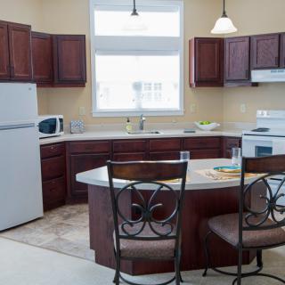 A modern kitchen interior featuring dark wood cabinets, a central island counter with chairs, and essential appliances like a stove, refrigerator, and microwave.