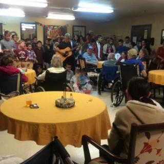 A group of people gathered indoors, some in wheelchairs, enjoying a musical performance.