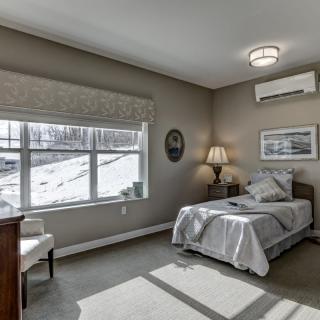 A minimalist bedroom with a single bed, large window, and neutral colors.