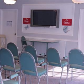 An empty meeting room with rows of chairs facing a large television screen.