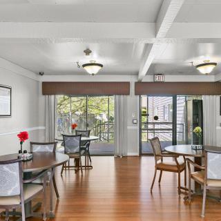 A bright and spacious dining area with wooden floors, featuring several tables and chairs, decorated with flowers.