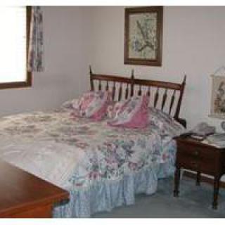 A cozy bedroom featuring a double bed with floral bedding and pillows, complemented by a wooden nightstand and framed artwork on the wall.