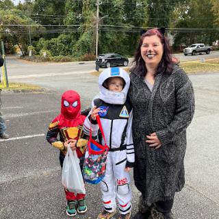 Two children in costumes, one as Spider-Man and the other as an astronaut, pose with a woman outdoors.