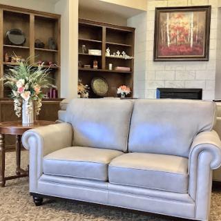A cozy living room setting featuring a light gray couch, decorative shelves, and a vase of flowers.