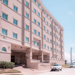 Exterior view of a hotel building with multiple floors and parked vehicles.
