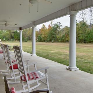 A peaceful porch with rocking chairs overlooking a grassy area.