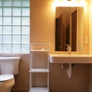 A bathroom interior with a sink, toilet, mirror, and shelving unit.