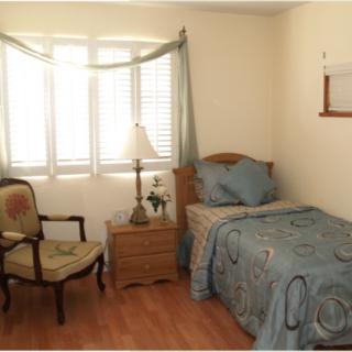 A cozy bedroom with a single bed, chair, and window with curtains.