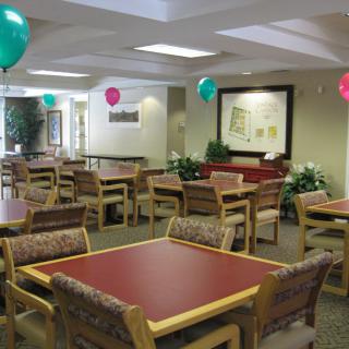 A decorated dining area with tables and chairs, featuring colorful balloons.