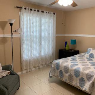 A cozy bedroom with a bed, nightstand, and armchair, featuring a window with sheer curtains.
